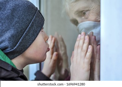 A sad grandmother mature woman in a respiratory mask communicates with grandchild through a window. Elderly quarantined, isolated. Pandemic coronavirus covid-19. Older people. Visit to grandma