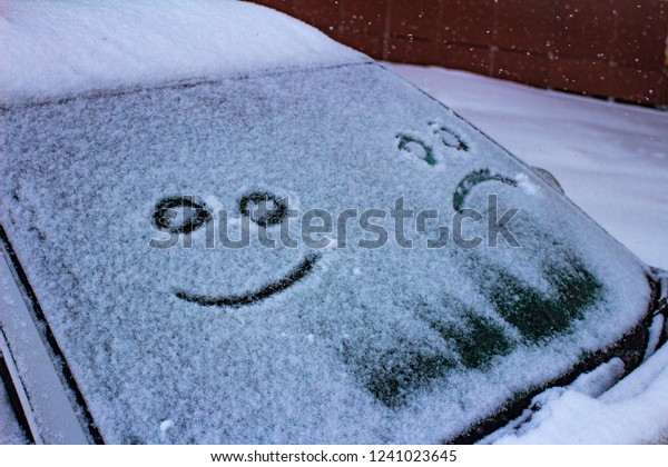 the sad and the happy smile on the snowy windshield\
of a car