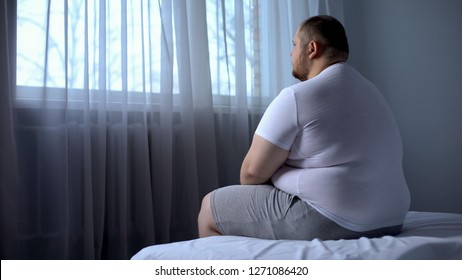 Sad heavy man sitting on bed at home, health problem, depression, insecurities