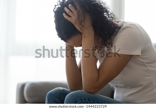 Sad hopeless young black woman sit alone at home\
feeling desperate depressed, upset stressed african girl suffer\
from alcohol abuse drug addiction, dependency, grief or guilt\
troubled with problems