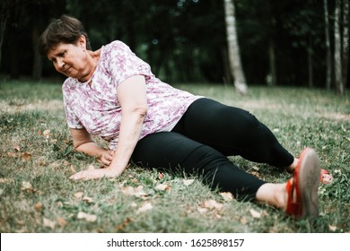 Sad And Hurt Senior Woman Lying On The Ground After Falling In The Park - Fragile Old Lady Sitting Down After Fainting - Elderly Person With Heart Problems In Need For Help