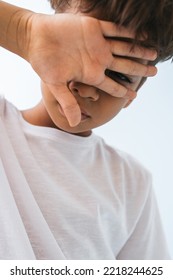 Sad Indian Boy Covering His Face With A Hand Against Bluish White Background. He Is Wearing White T Shirt. Looking Down. Close Up.