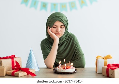 Sad Indian Teen Girl In Hijab Having Dull Birthday Party, Feeling Bored, Celebrating Holiday Alone During Coronavirus Isolation. Unhappy Muslim Teenager Disliking Lonely B-day Celebration At Home