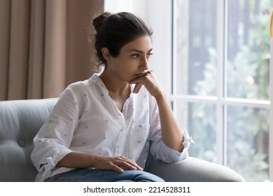 Sad Indian woman sit on armchair looks concerned, feels confused, thinks, search solution in difficult life situation, hesitating seated alone at home. Relations problems, break up and marriage split - Powered by Shutterstock