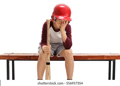 Sad Kid With A Baseball Bat And A Helmet Sitting On A Bench And Holding His Head In Disbelief Isolated On White Background