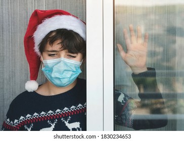 Sad Kid With Medical Mask Wearing Santa Claus Hat Wait For Santa Claus Next To A 
Window In Christmas By The Coronavirus Pandemic