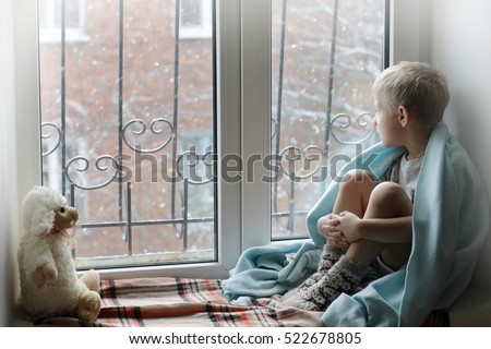 Sad kid on window cannot go out because of cold and snow