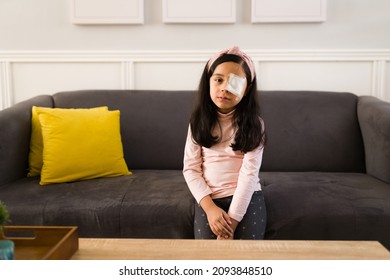 Sad Kid With Poor Eyesight Wearing An Eye Patch And Looking At The Camera While Resting On The Sofa 