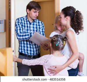 Sad Landlord Standing Indoors And Asking Family Of Tenants For Money