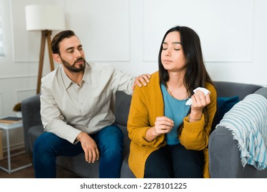 Sad latin woman crying using a tissue while arguing with her upset husband trying to talk about their marriage problems - Shutterstock ID 2278101225