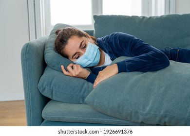 Sad latin woman with protective face mask at home living room couch feeling tired and worried suffering depression amid coronavirus lockdown and social distancing. Mental Health and isolation concept.