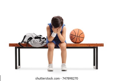 Sad little basketball player sitting on a bench and crying isolated on white background