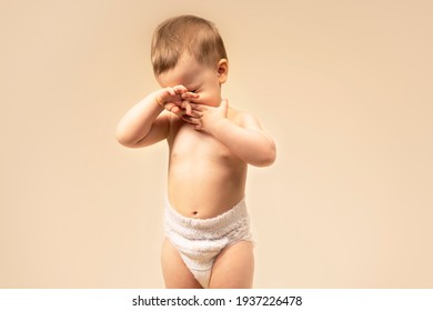 Sad Little Boy Crying, Rubbing His Eyes With His Hands. Allergies Or Tears In A Baby. Itchy, Child Itchy Eyes Baby Wearing Diapers. On A Solid Background Monochromatic In The Studio