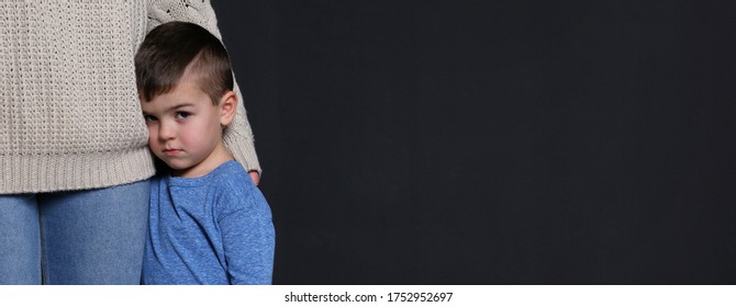 Sad little boy hugging his mother on black background, banner design with space for text. Time to visit child psychologist
