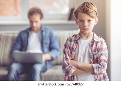 Sad little boy is looking at camera while his father is working in the background