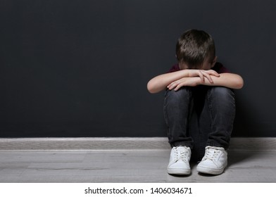 Sad Little Boy On Floor Near Black Wall. Space For Text