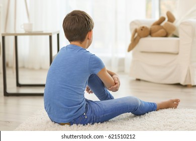 Sad Little Boy Sitting On Floor In Room