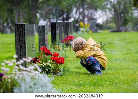 Sad little child, blond boy, standing in the rain on cemetery, sad person, mourning, summer rainy day