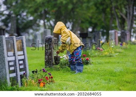 Sad little child, blond boy, standing in the rain on cemetery, sad person, mourning, summer rainy day