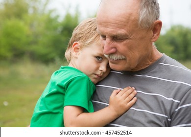 Sad little child, boy, hugging his grandfather at outdoors. Family concept