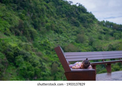 Sad little child girl lying down on brown wooden bench alone. - Powered by Shutterstock