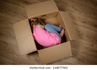 A Sad Little Child Lies In A Box On The Floor. The Concept Of Isolation, Loneliness, Running Away From Problems.