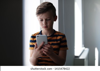 Sad Little Child With Smartphone Indoors. Danger Of Internet