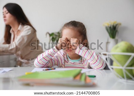 Sad little daughter with working mother at home