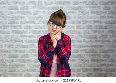 Sad little girl with earache on a brick wall background. Ear ache concept. Child has a sore ear. Little girl suffering from otitis. Cute little  girl suffering from severe pain in the Ear.