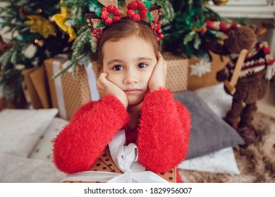 Sad Little Girl With Gift Box Sitting Near Christmas Tree.