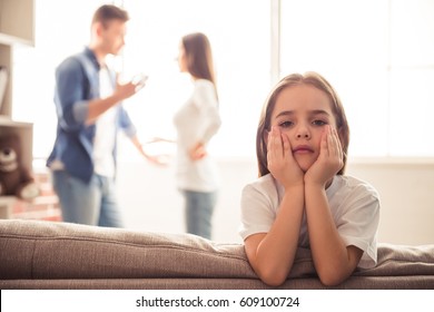 Sad little girl is looking at camera while her parents are arguing in the background