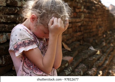 Sad little girl on the background of an old brick wall