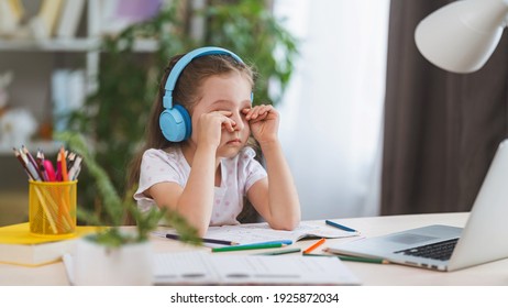 sad little girl, schoolgirl wearing headphones, uses laptop to study at home. child is bored to learn and gain knowledge remotely. student wants to go to school. digital concept e-learning. - Shutterstock ID 1925872034
