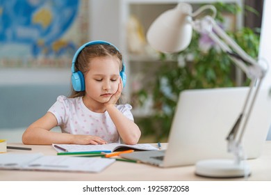 sad little girl, schoolgirl wearing headphones, uses laptop to study at home. child is bored to learn and gain knowledge remotely. student wants to go to school. digital concept e-learning. Remote.