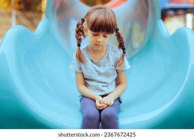 
Sad Little Girl Sitting Alone in a Playground Slide. Timid anxious single child having none to play with
