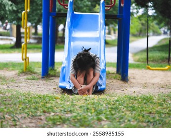 A sad little girl is sitting alone on a playground slide. An unhappy child is playing alone. - Powered by Shutterstock