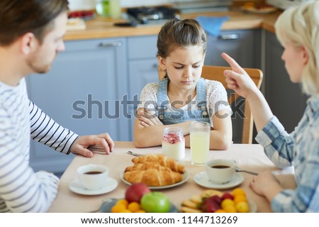 Sad little girl sitting by table while mother forbidding her to have dessert because of bad behavior