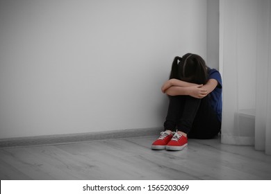 Sad little girl sitting on floor indoors, space for text. Child in danger - Shutterstock ID 1565203069