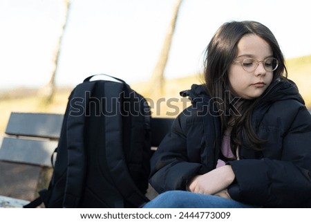 Sad little girl sitting on a bench in the park and looking at camera