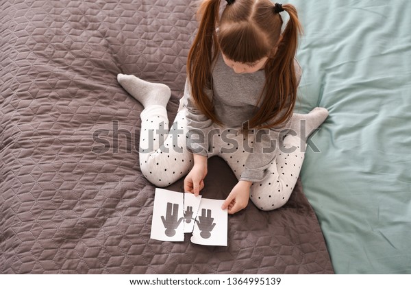 Sad little girl with torn picture of family\
sitting on bed. Concept of\
divorce