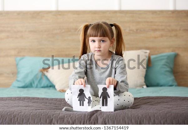 Sad little girl with torn picture of family at\
home. Concept of divorce