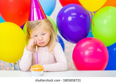 Sad Little Girl Wearing  Party's Cap Sits With Birthday Cupcake 