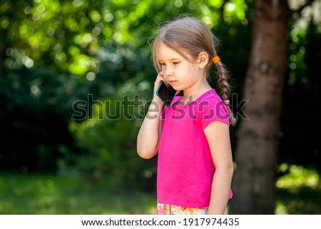 Sad lone little school age girl, child talking on the phone, smartphone outside. Unhappy, downhearted kid alone, phone call sad news, loneliness concept. Outdoors lifestyle shot, copy space, closeup
