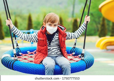 Sad Lonely Boy. Bored Child At Empty Playground. Quarantine. Child Wearing Safety Mask Outdoors. Sad Boy In Face Mask Sitting On Swing Alone. Coronavirus Prevention.  Real Life 2020.