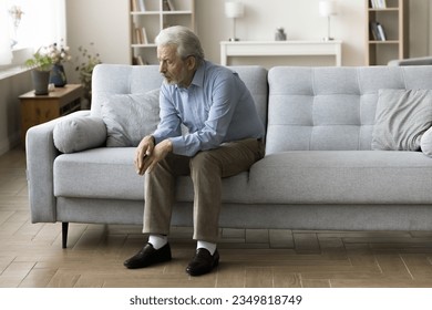 Sad lonely old grey haired man sitting alone on home sofa, looking down in bad thought, suffering from depression, apathy, coping with loss, bad news about healthcare, family problems