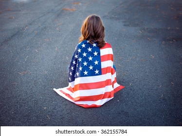 Sad lonely patriot woman sitting down with the american flag wrapped around her. Deployment, military life and relationship concept