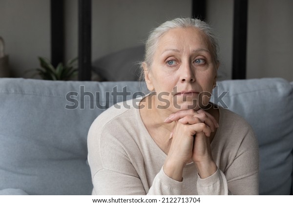 Sad lonely pensive elder lady looking away,\
sitting on couch at home with chin on hands, thinking over health\
problems, feeling sadness, boredom, apathy, concerned about memory\
loss, dementia