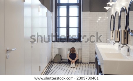 Sad and lonely teen girl sit on restroom floor alone. Portrait of stressed teenage schoolgirl sitting on floor in toilet feeling depressed