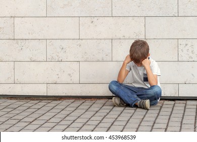 Sad, Lonely, Unhappy, Disappointed Child Sitting Alone On The Ground. Boy Holding His Head, Look Down. Outdoor