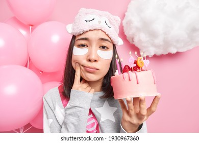 Sad Lonely Woman Forces Smile Feels Upset About Getting Older Holds Delicious Strawberry Cake Celebrates Birthday Alone Dressed In Nightwear Poses Near Balloons Isolated Over Pink Background